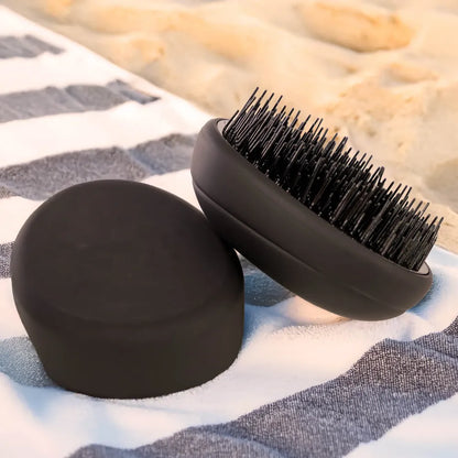 PUR HAIR Detangler Brush, in schwarz, liegt auf gestreiftem Handtuch, am Strand