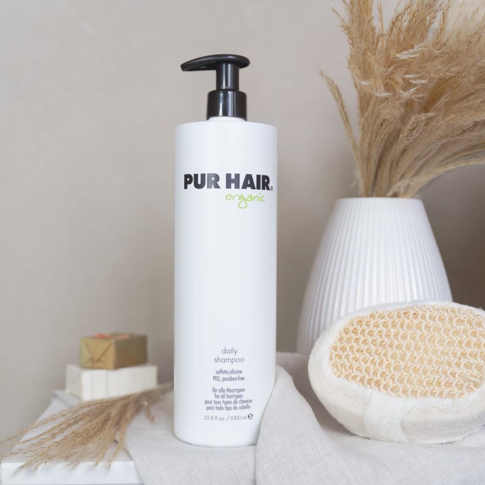 Weiße Flasche PUR HAIR Organic Daily Shampoo, 1000 ml, auf grauem Tuch mit  Trockenblumen im Badezimmer platziert