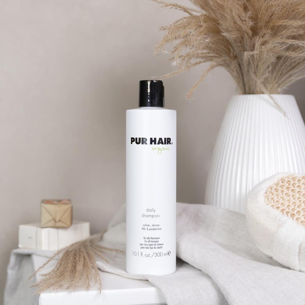 Weiße Flasche PUR HAIR Organic Daily Shampoo, 300 ml, auf grauem Tuch mit  Trockenblumen im Badezimmer platziert
