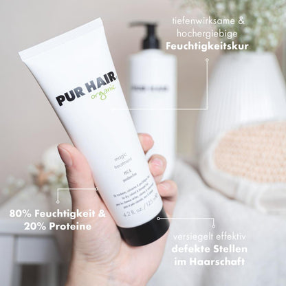 PUR HAIR Organic Magic Treatment in 125 ml Tube wird in der Hand gehalten, im Hintergrund weiße Blüten und eine große Flasche; Text weist auf Feuchtigkeitspflege, 80 % Feuchtigkeit, 20 % Proteine, versiegelt effektiv defekte Stellen am Haar