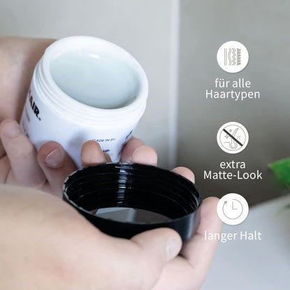 PUR HAIR Styling-Paste in offener Dose, gehalten in zwei Händen. Eigenschaften: für alle Haartypen geeignet, extra Matte-Look, langer Halt