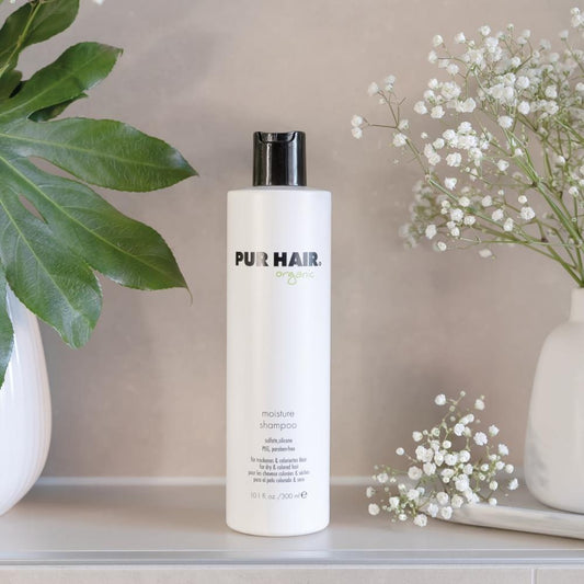 PUR HAIR Organic Moisture Shampoo, 300 ml Flasche in Weiß mit schwarzem Deckel, neben Vase mit Blumen