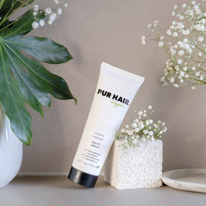 PUR HAIR Organic Moisture Treatment steht angelehnt an einem weißen Steinblock, dokoriert mit Trockeblumen