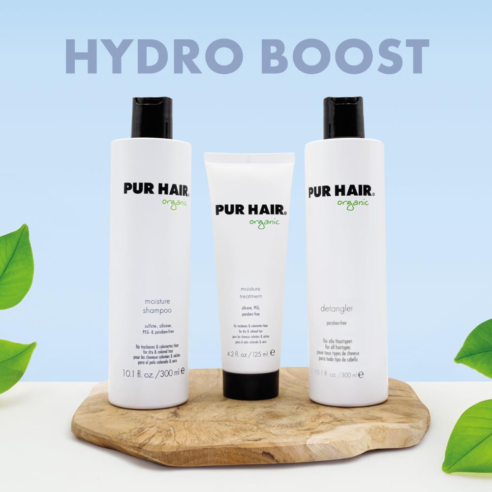 PUR HAIR Organic Naturgelocktes und Trockenes Haar Set bestehend aus Moisture Shampoo, Moisture Treatment und Detangler. Die drei weißen Flaschen und Tuben stehen dekorativ auf einem Holzbrett vor einem pastell-blau Hintergrund mit der Aufschrift ‚Hydro Boost‘